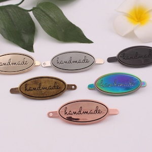 May include: Six oval-shaped metal tags with the word "handmade" engraved on them. The tags are in different colors: gold, silver, black, rainbow, and rose gold.