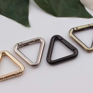 Puede incluir: Cuatro cierres metálicos en forma de triángulo en oro, plata, negro y bronce.