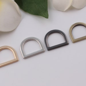 May include: Four D-rings in different finishes: gold, silver, black, and antique brass. The rings are all the same size and shape.