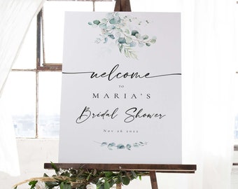 May include: A white welcome sign with green eucalyptus leaves and the text "Welcome to Maria's Bridal Shower Nov 26 2022".