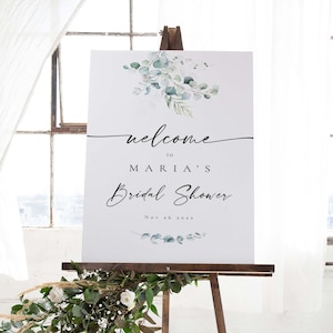 May include: A white welcome sign with green eucalyptus leaves and the text "Welcome to Maria's Bridal Shower Nov 26 2022".