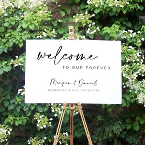 May include: White wedding welcome sign with black calligraphy text that reads "Welcome to our forever Megan & Daniel So glad you're here | 07.15.2023"