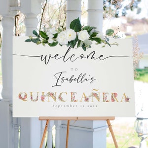 May include: A white welcome sign with floral accents and gold lettering. The sign reads "Welcome to Isabella's Quincea&ntilde;era September 12, 2022".