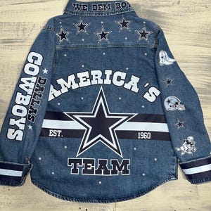 May include: A blue denim button-down shirt featuring Dallas Cowboys graphics. The back displays a large star, the text "AMERICA'S TEAM," "EST. 1960," and "WE DEM BOYZ" on the collar. Sleeves feature football helmet, boot, and player icons.
