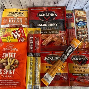 Peut inclure: Assortiment d'en-cas emball&eacute;s, dont du jerky de b&oelig;uf, du jerky de bacon, des b&acirc;tonnets de saucisse et un m&eacute;lange montagnard. Les marques incluent Jack Link's, Slim Jim, Tillamook et Nature's Garden. Les collations sont de couleurs vari&eacute;es.