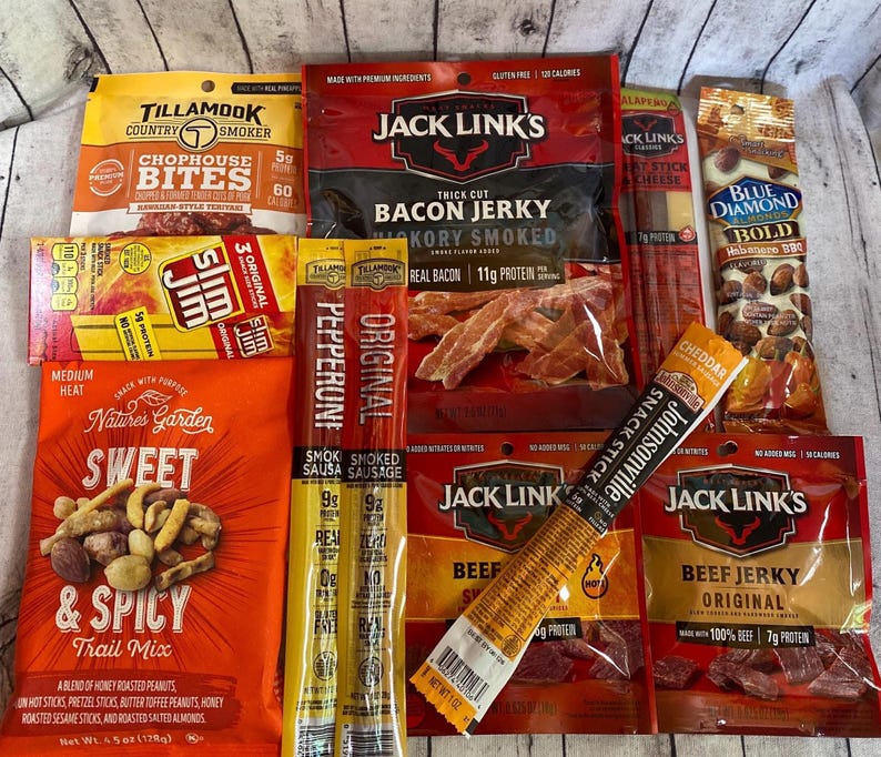 Peut inclure: Assortiment d'en-cas emball&eacute;s, dont du jerky de b&oelig;uf, du jerky de bacon, des b&acirc;tonnets de saucisse et un m&eacute;lange montagnard. Les marques incluent Jack Link's, Slim Jim, Tillamook et Nature's Garden. Les collations sont de couleurs vari&eacute;es.