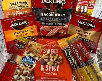 May include: A collection of packaged snacks, including beef jerky, bacon jerky, trail mix, and snack sticks. The brands include Jack Link's, Slim Jim, Tillamook, Blue Diamond, and Nature's Garden. The packaging is primarily red, orange, and yellow.