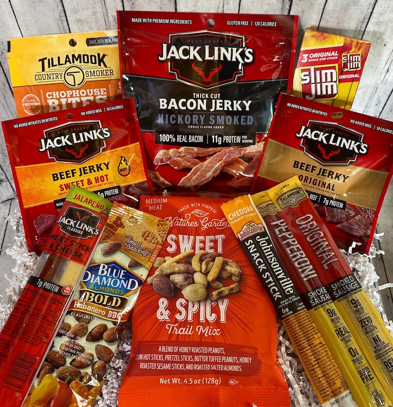 Peut inclure: Un assortiment d'en-cas emball&eacute;s, dont du jerky de b&oelig;uf, du jerky de bacon, du m&eacute;lange montagnard et des b&acirc;tonnets de collation. Les marques incluent Jack Link's, Slim Jim, Tillamook, Blue Diamond et Nature's Garden. L'emballage est principalement rouge, orange et jaune.