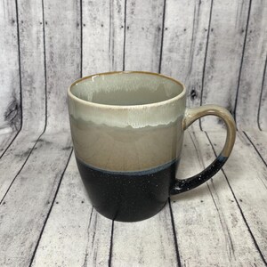 以下が含まれることがあります： 黒い斑点のあるベースからベージュとクリーム色に変化し、茶色の縁が付いたセラミックコーヒーマグ。ハンドルはベージュで、黒い斑点が付いています。マグカップは温かい飲み物用に設計されています。