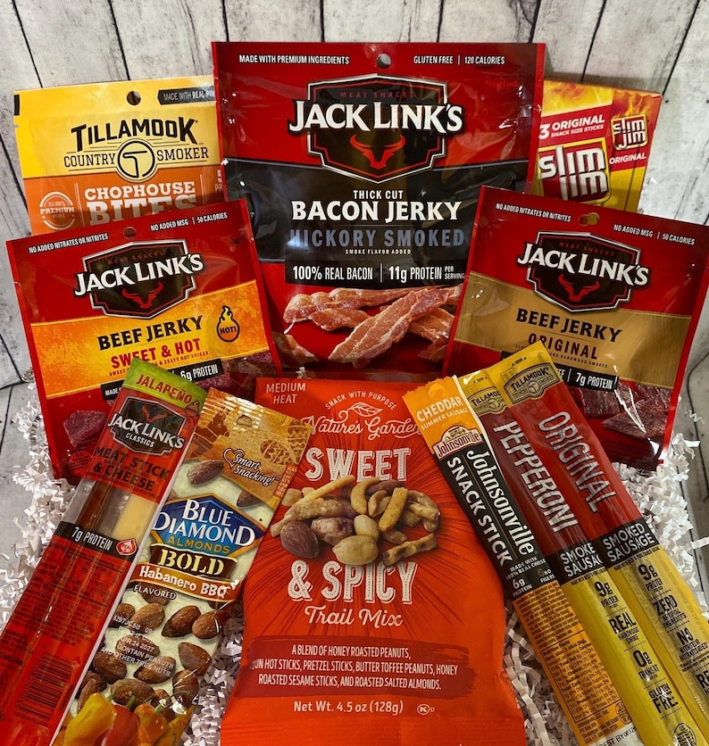 Peut inclure: Un panier cadeau rempli de diverses collations sal&eacute;es. L'assortiment comprend du jerky, du m&eacute;lange montagnard, des b&acirc;tonnets de collation et des Slim Jim. Des marques comme Jack Link's, Tillamook et Blue Diamond sont visibles. L'emballage pr&eacute;sente des couleurs vives et des descriptions de produits.