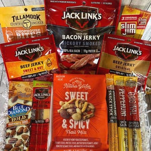 Peut inclure: Un assortiment d'en-cas emball&eacute;s, comprenant du jerky, du m&eacute;lange montagnard et des b&acirc;tonnets de collation. Les marques incluent Jack Link's, Tillamook, Slim Jim, Blue Diamond et Nature's Garden. L'image pr&eacute;sente divers go&ucirc;ts et types d'en-cas.