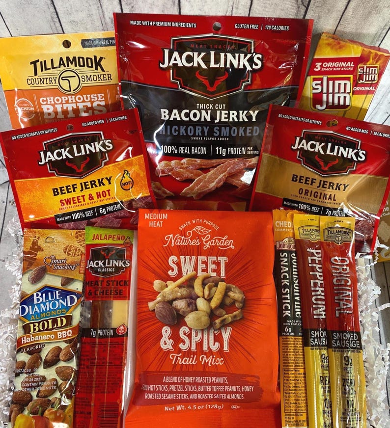 Peut inclure: Un assortiment d'en-cas emball&eacute;s, comprenant du jerky, du m&eacute;lange montagnard et des b&acirc;tonnets de collation. Les marques incluent Jack Link's, Tillamook, Slim Jim, Blue Diamond et Nature's Garden. L'image pr&eacute;sente divers go&ucirc;ts et types d'en-cas.