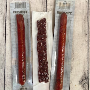 Peut inclure: Trois paquets de collations de viande. Deux paquets contiennent de longs b&acirc;tonnets de viande cylindriques, rouge-brun. Le troisi&egrave;me paquet contient une bande de jerky brun fonc&eacute;. Tous les paquets sont scell&eacute;s et &eacute;tiquet&eacute;s avec les logos "BEAST" et "ICON MEATS".