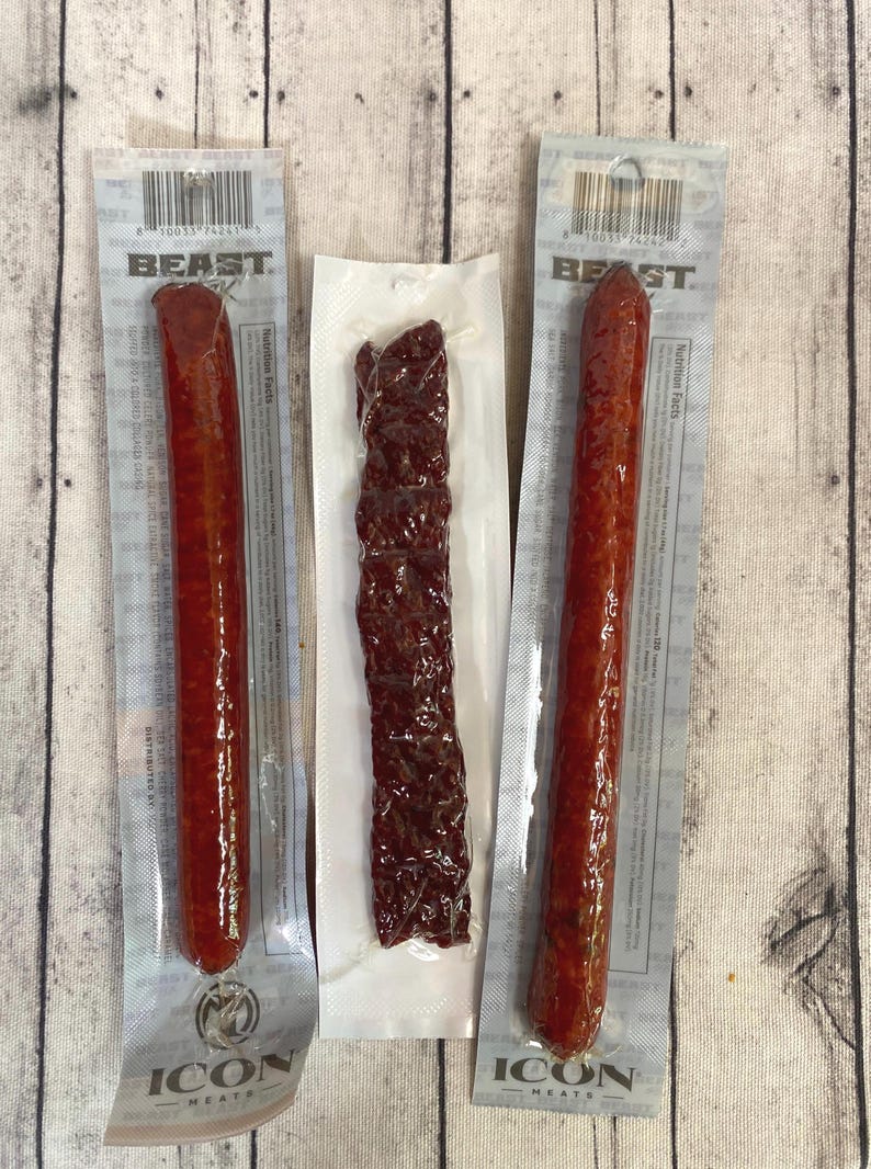 Peut inclure: Trois paquets de collations de viande. Deux paquets contiennent de longs b&acirc;tonnets de viande cylindriques, rouge-brun. Le troisi&egrave;me paquet contient une bande de jerky brun fonc&eacute;. Tous les paquets sont scell&eacute;s et &eacute;tiquet&eacute;s avec les logos "BEAST" et "ICON MEATS".