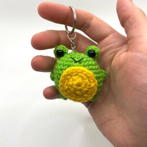 May include: Green crocheted frog keychain with black eyes and a yellow crocheted belly.