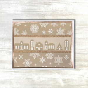 Comparta cálidos deseos con un acogedor copo de nieve y una encantadora tarjeta de felicitación de pueblo, terminada con papel brillante para darle un toque elegante hecho a mano.