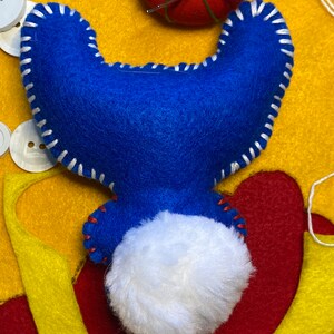 May include: A blue felt toy with white stitching and a white fluffy tail. The toy is lying on a yellow and red felt surface.