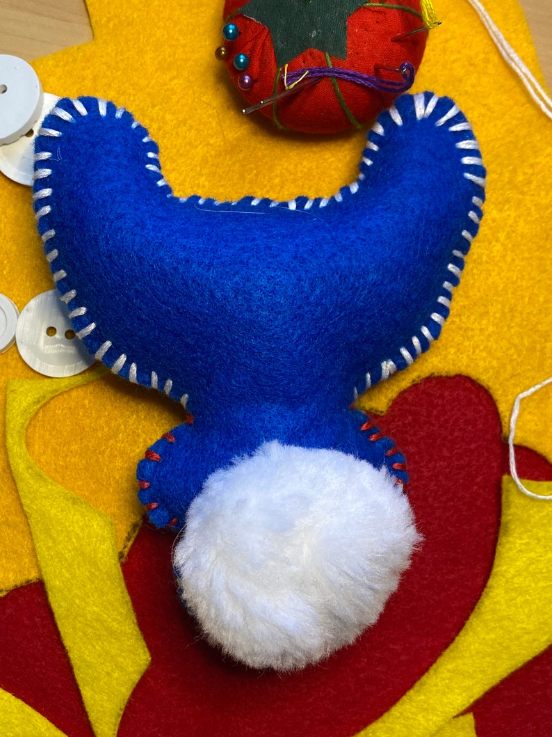 May include: A blue felt toy with white stitching and a white fluffy tail. The toy is lying on a yellow and red felt surface.