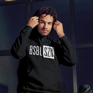 May include: Black hoodie with the text "BSBL SZN" in white block letters. The hoodie has a drawstring hood and a front pocket. The person in the image is wearing the hood.
