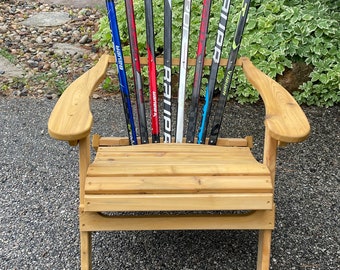 May include: A wooden chair with a back made of hockey sticks. The chair is made of natural wood and has a rustic look. The chair is sitting on a gravel driveway.