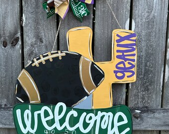 Peut inclure: Un porte-manteau en bois avec un numéro 4 jaune, un ballon de football noir et or et une pancarte d'accueil verte avec les chiffres 30, 40, 50, 40 et 30. Le porte-manteau est décoré d'un nœud violet et or.