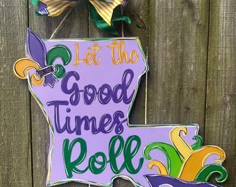 Może przedstawiać: Drewniany wieszak na drzwi w kształcie Luizjany, w kolorze fioletowym i zielonym, z napisem "Let the Good Times Roll" i ozdobami w stylu Mardi Gras.