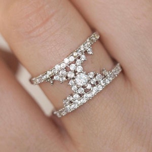 May include: A silver ring with a double band design. The ring is set with small, clear cubic zirconia stones that form a geometric pattern.