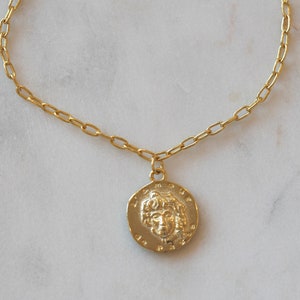 May include: A gold chain necklace with a round pendant featuring a detailed profile of a woman's face.
