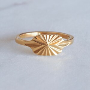 Könnte beinhalten: Ein goldener Ring mit einem geometrischen, sternenförmigen Design. Der Ring ist aus Metall gefertigt und hat eine glatte, polierte Oberfläche.