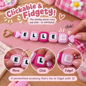 May include: A pink and white fidget keyring featuring square, clickable blocks spelling the name ELLE with a paw print icon. The accessory includes a gold heart-shaped clasp and pink cord. Text on the image reads Clickable & Fidgety!