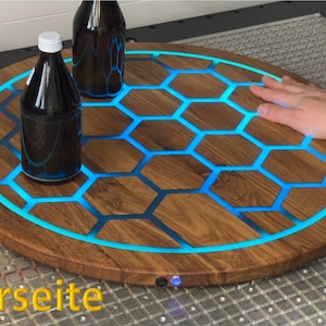 Könnte beinhalten: Ein runder Serviertablett aus Holz mit einem wabenförmigen Design, das von blauen LED-Leuchten beleuchtet wird. Zwei dunkle Flaschen mit weißen Verschlüssen stehen auf dem Tablett. Der Durchmesser des Tabletts beträgt ca. 46 cm.