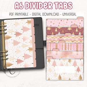 May include: A6 divider tabs with a Christmas theme. The tabs feature pink and gold designs, including Christmas trees, stars, and geometric patterns. The tabs are shown inside a black planner. Text on the image reads "A6 DIVIDER TABS".