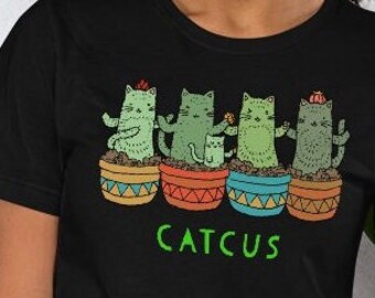 May include: Black t-shirt featuring a graphic of four cats in pots, resembling cacti. The text "CATCUS" is printed below the graphic.