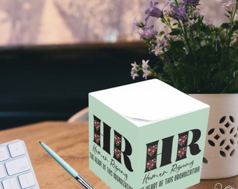 May include: A mint green cube-shaped sticky note holder with the text "HR Human Resources The Heart of This Organisation" printed on two sides. The text is in black with a floral design behind it.