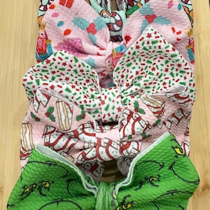 May include: A collection of festive hair bows. The bows feature holiday patterns including candy canes, gifts, holly, and a green Grinch design. The bows are arranged on a wooden surface.