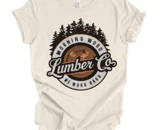 May include: A cream colored t-shirt with a black and orange logo that says "Morning Wood Lumber Co. We Work Hard". The logo features a stylized tree and a circular design.
