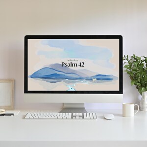 May include: A computer screen displaying a watercolour landscape with a blue mountain range, a winding river, and the text "As the deer... Psalm 42".