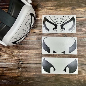 May include: Four black and white vinyl stickers featuring different designs. The stickers are on a wooden surface. The designs include a spider web, two eyes, and a pair of fangs.