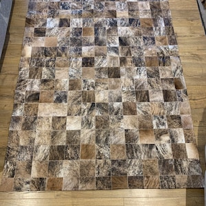 May include: A patchwork cowhide rug with a square pattern in shades of brown, black, and white.