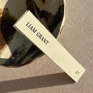 May include: A beige place card with the text "LIAM GRANT" and the number "27" printed in black.