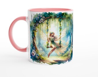 May include: A white ceramic mug with a pink rim features a colorful illustration of a fairy with wings sitting on a swing in a forest setting. The fairy is wearing a green dress and has long blonde hair.