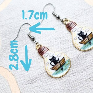 May include: A pair of gold lightbulb earrings with a black cat in a boat design. The earrings are 2.8 inches long and 1.7 inches wide.