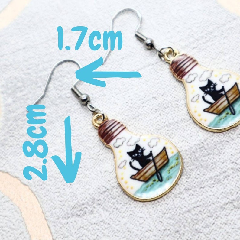 May include: A pair of gold lightbulb earrings with a black cat in a boat design. The earrings are 2.8 inches long and 1.7 inches wide.