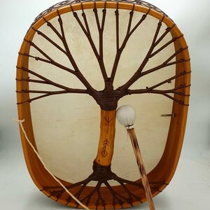 Puede incluir: Un tambor de marco de madera con una cabeza de cuero marr&oacute;n y un dise&ntilde;o de &aacute;rbol de la vida. El tambor est&aacute; decorado con un patr&oacute;n marr&oacute;n y blanco alrededor del borde. Se incluye un mazo de madera con una cabeza blanca.