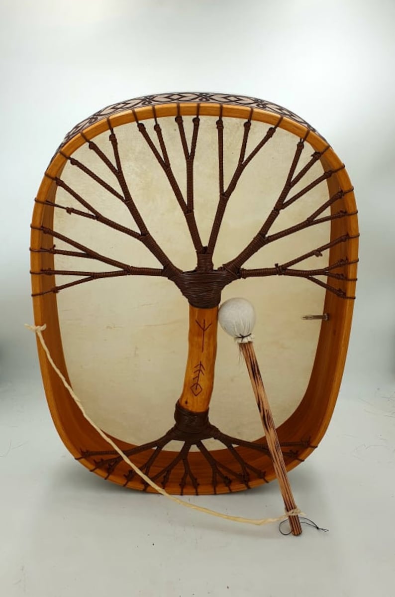 Puede incluir: Un tambor de marco de madera con una cabeza de cuero marr&oacute;n y un dise&ntilde;o de &aacute;rbol de la vida. El tambor est&aacute; decorado con un patr&oacute;n marr&oacute;n y blanco alrededor del borde. Se incluye un mazo de madera con una cabeza blanca.
