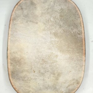 Puede incluir: Un tambor de cuero marr&oacute;n claro de gran tama&ntilde;o, de forma ovalada, con un borde ligeramente elevado.