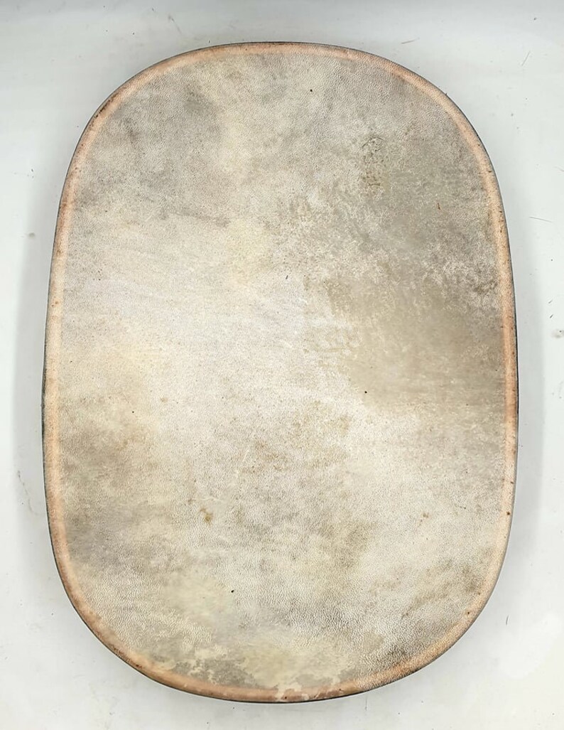 Puede incluir: Un tambor de cuero marr&oacute;n claro de gran tama&ntilde;o, de forma ovalada, con un borde ligeramente elevado.