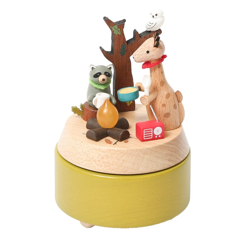 May include: Wooden music box with a giraffe, raccoon, and owl figurine. The giraffe is holding a bowl and the raccoon is holding a cup. The music box is playing a song about camping.