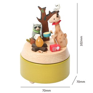 May include: Wooden music box with a giraffe, raccoon, and owl figurine. The music box is green and has a wooden base. The figures are around a campfire with a radio. The music box measures 7 inches in diameter and 4 inches in height.