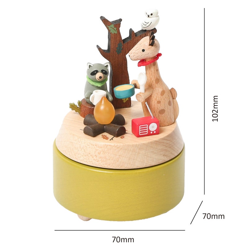 May include: Wooden music box with a giraffe, raccoon, and owl figurine. The music box is green and has a wooden base. The figures are around a campfire with a radio. The music box measures 7 inches in diameter and 4 inches in height.